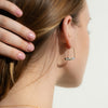 Close-up of a person wearing a delicate arch earring with small stones.