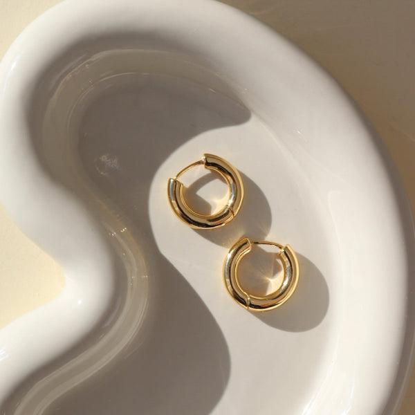 Gold hoop earrings on a white ceramic dish