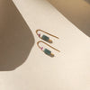 Pair of gold threader earrings with green and pink natural stones on a beige surface