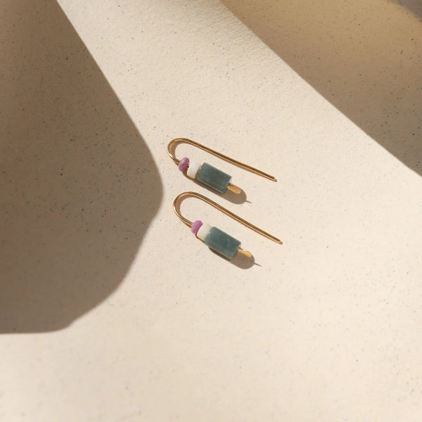Pair of gold threader earrings with green and pink natural stones on a beige surface