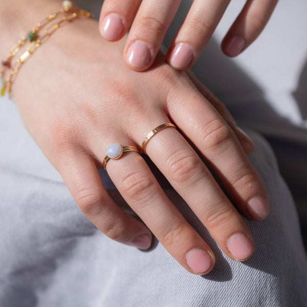 Close-up of a hand wearing a gold ring with a small stone on a light background