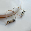 Pair of gold arch earrings with cylindrical beads on a light background