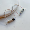 Pair of silver earrings with cylindrical beads on a light background