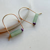 Gold arch earrings with green and purple beads on a light background