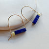 Gold arch earrings with blue and yellow cylindrical beads on a light background