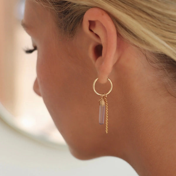 Close-up of person wearing a gold hoop earring with amethyst stone and gold chain dangle.