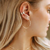 Close-up of a woman's ear with gold hoop earrings and a small stud.