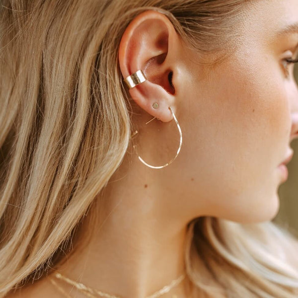 Close-up of a woman's ear with gold hoop earrings and a small stud.