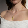 Close-up of person wearing a light yellow-green serpentine pendant on a delicate gold chain necklace.