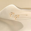 Gold wishbone shaped stud earrings on neutral background.