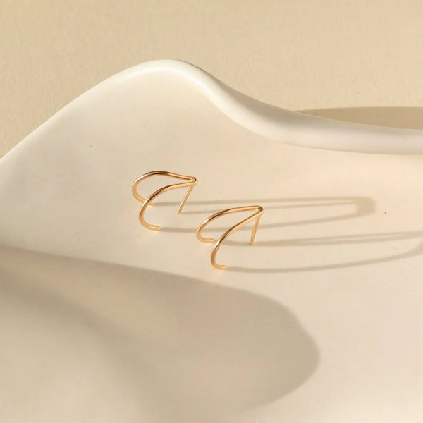 Gold wishbone shaped stud earrings on neutral background.