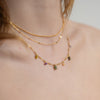 Gold necklaces with gemstones on a person's neck against a neutral background