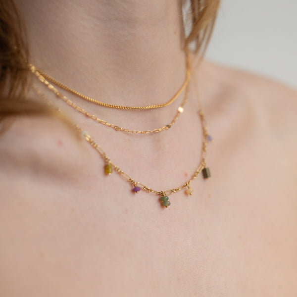 Gold necklaces with gemstones on a person's neck against a neutral background