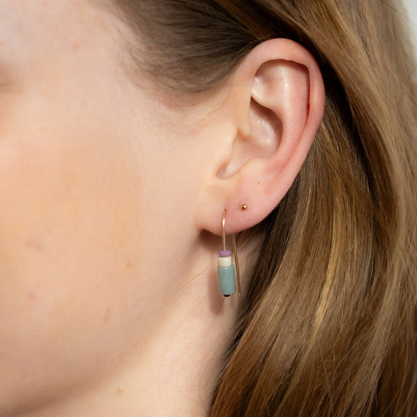 Close-up of an ear wearing a gold threader earring with natural purple, white, and green stones.