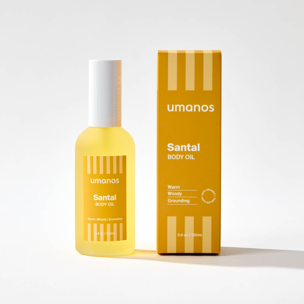 Yellow bottle and box of umanos Santal Body Oil on a white background