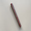 A taper candle in a red and green vertical striped design against a neutral backdrop.