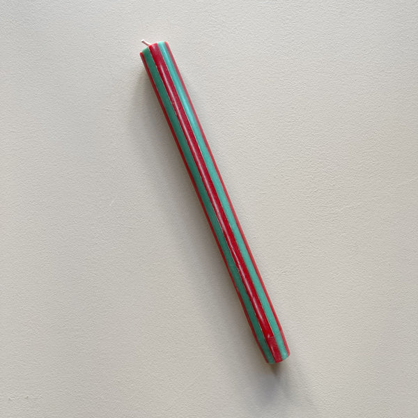A taper candle in a red and green vertical striped design against a neutral backdrop.