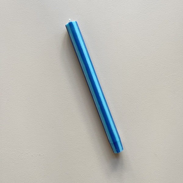 A taper candle in a sky blue and navy vertical striped design against a neutral backdrop.
