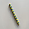 A taper candle in a grey and yellow vertical striped pattern against a neutral backrop.