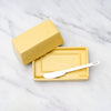 Yellow butter dish with a stainless steel butter knife on a marble surface