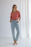 Woman wearing a pink shirt and light blue jeans standing against a white curtain.