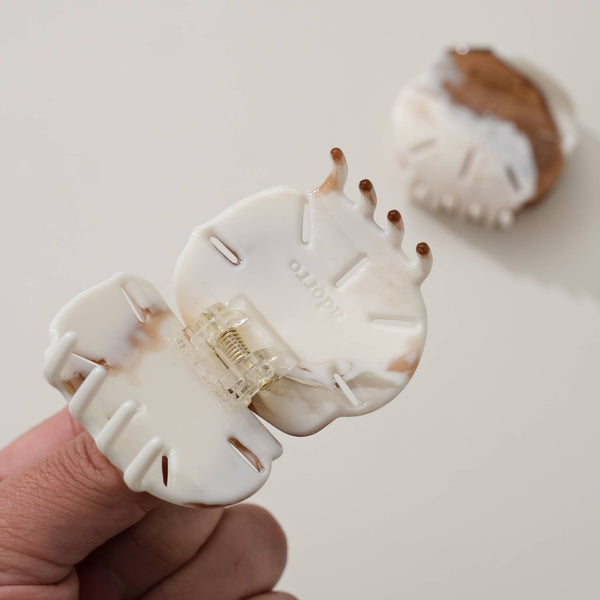 White hair clip held by a hand with a blurred background