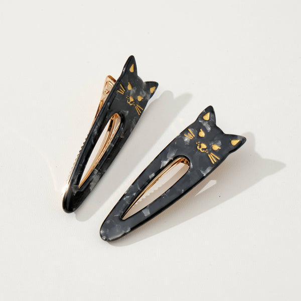 Two black cat-shaped hair clips with gold accents on a white background