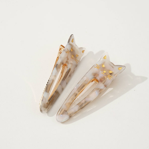 Pair of cat shaped taupe tortoiseshell hair clips with gold accents on a light beige background