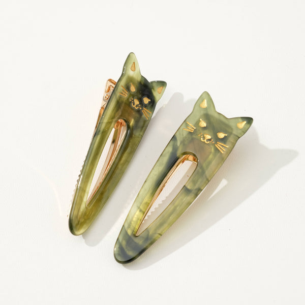 Two green cat-shaped hair clips on a white background