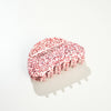 A curve shaped hair claw in white with red speckles photographed on a white surface with a soft shadow.