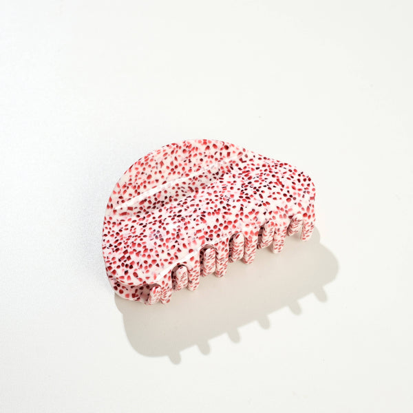 A curve shaped hair claw in white with red speckles photographed on a white surface with a soft shadow.