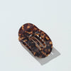An oval hair claw clip with a glossy dark brown tortoiseshell pattern, shown on a clean white background with a soft shadow.