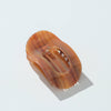 A translucent oval hair claw clip in warm amber-brown tones, photographed on a clean white background with a soft shadow.