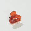 A translucent amber-brown mini oval hair claw clip on a clean white background with a soft shadow.