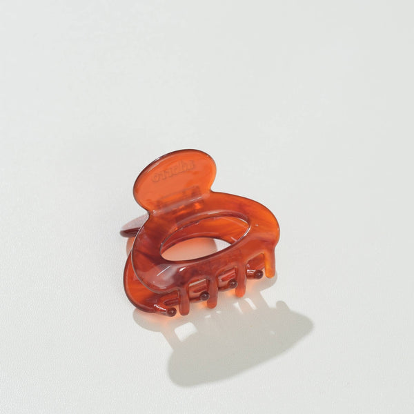 A translucent amber-brown mini oval hair claw clip on a clean white background with a soft shadow.