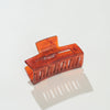 An amber translucent rectangular hair claw clip on a clean white background with a soft reflection underneath.