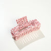 A large rectangular hair claw in white with red speckles photographed on a white surface with a soft shadow.
