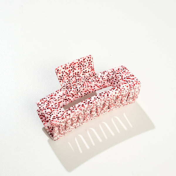 A large rectangular hair claw in white with red speckles photographed on a white surface with a soft shadow.