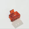 A mini rectangular translucent amber-brown hair claw clip on a clean white background with a soft shadow.