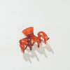 A translucent squiggle shaped amber-orange claw hair clip on a clean white background with soft shadows.
