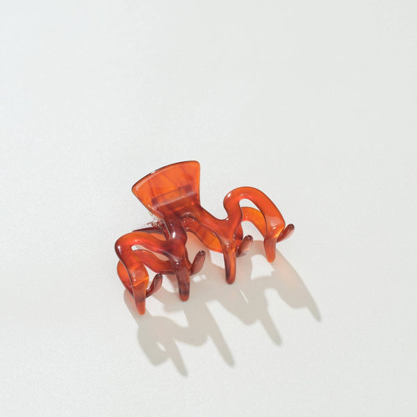 A translucent squiggle shaped amber-orange claw hair clip on a clean white background with soft shadows.