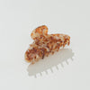 A tortoiseshell hair claw clip with a marbled amber, brown, and cream pattern, shown on a clean white background with a soft shadow.