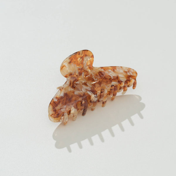 A tortoiseshell hair claw clip with a marbled amber, brown, and cream pattern, shown on a clean white background with a soft shadow.