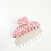 A large claw-style hair clip with a glossy white base covered in small red speckles, photographed on a clean white background with a soft shadow.