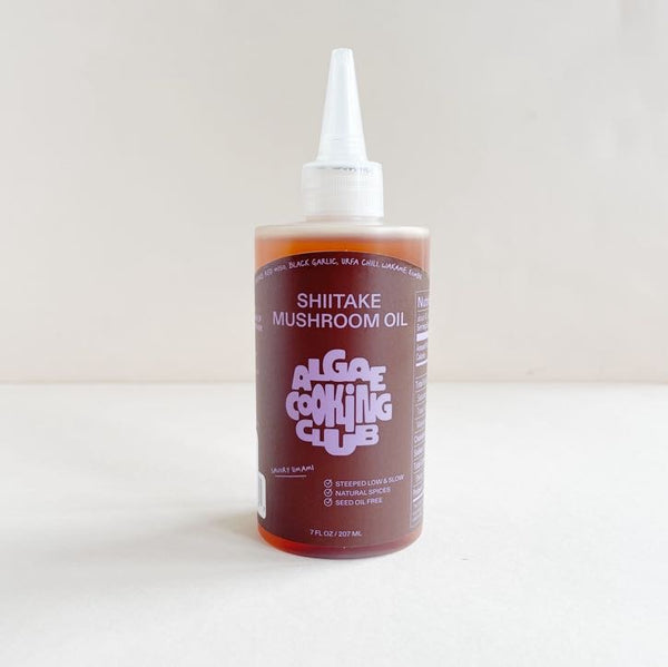 A bottle of Shiitake Mushroom Oil with a white cap on a light background.