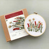 A hand embroidery kit shown with its kraft paper packaging box and a finished embroidery hoop displaying the embroidered floral design. The box reads 'Autumn Meadow Hand Embroidery Kit'.