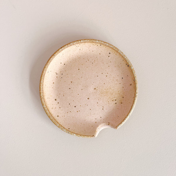 Glazed matte pink orange ceramic spoon rest on neutral background.