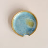 Glazed earthy blue and brown ceramic spoon rest on neutral background.