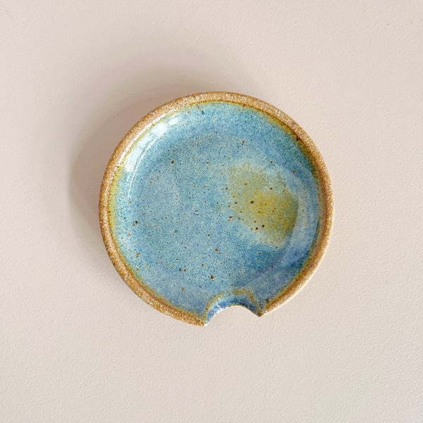 Glazed earthy blue and brown ceramic spoon rest on neutral background.