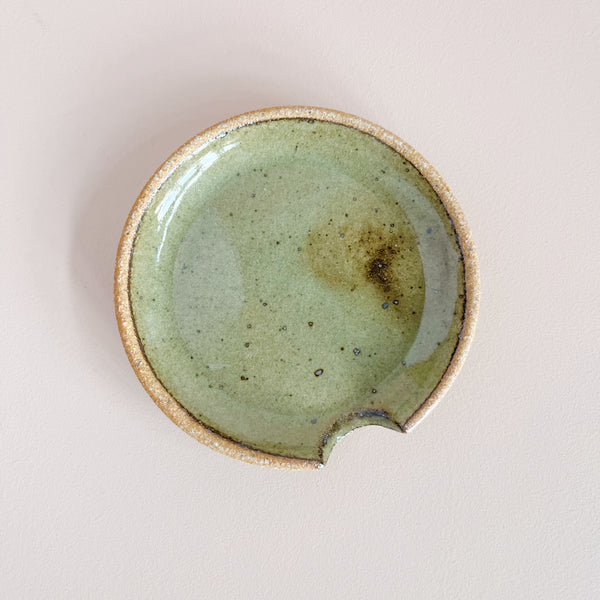 Earthy sage green ceramic spoon rest on netural background.